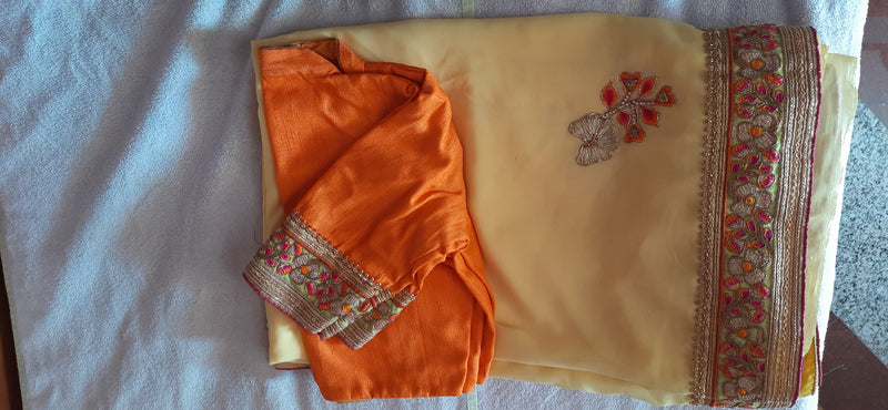 GAURI- A SOFT YELLOW GEORGETTE SAREE WITH BEAUTIFUL RUST AND GOLD EMBROIDERED BORDER AND SCATTERED FLORAL EMBROIDERY IN THE BODY, INCLUDES STITCHED BLOUSE