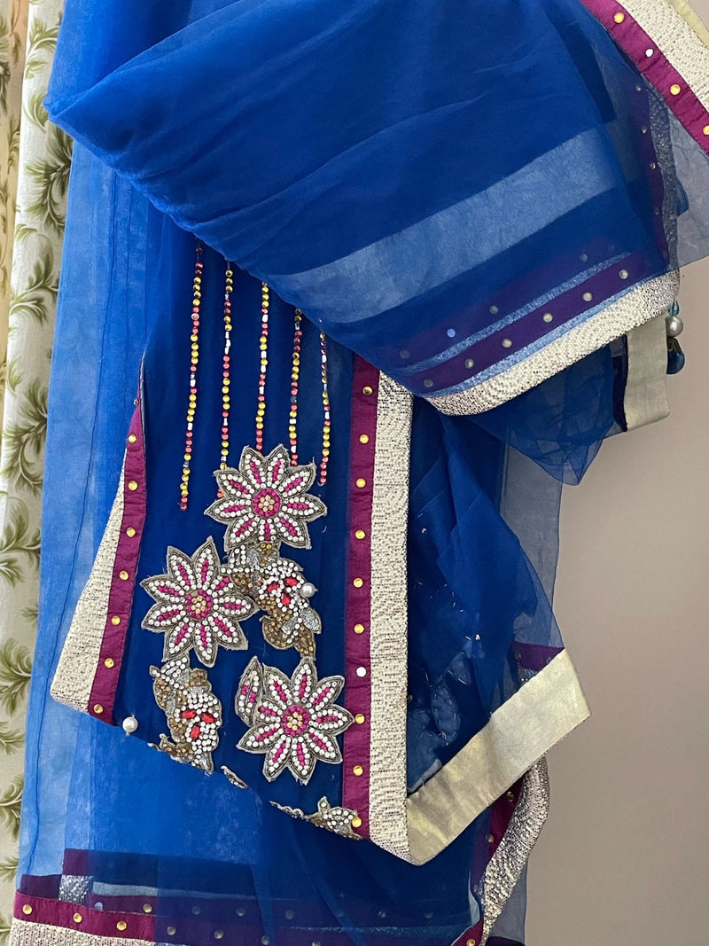 NAVYA NAVELI- A BEAUTIFUL NET SAREE IN BLUE WITH GOLDEN AND PINK BORDER BROOCH STYLE FLORAL WORK ON THE SHOULDER. COMES WITH A SATIN PETTICOAT WITH SEQUIN WORK ON IT AND A CONTRAST PINK AND MAROON STITCHED BLOUSE